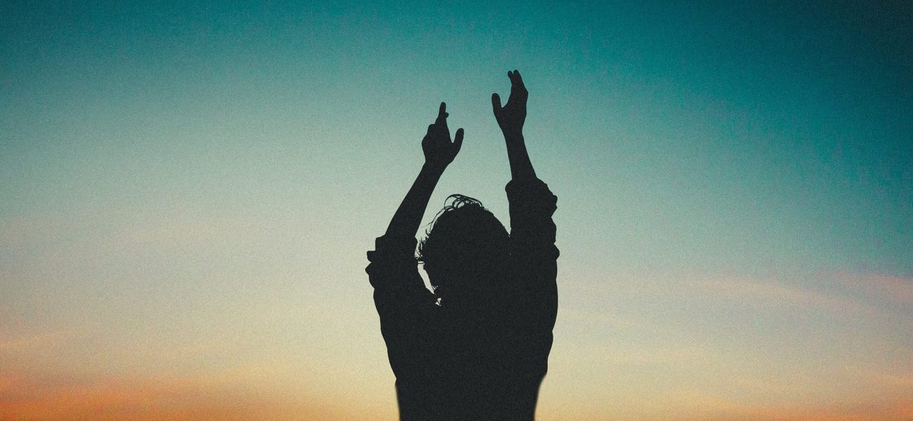 A person with upraised hands silhouetted against an evening sky, symbolising the benefits of meditation