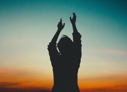 A person with upraised hands silhouetted against an evening sky, symbolising the benefits of meditation