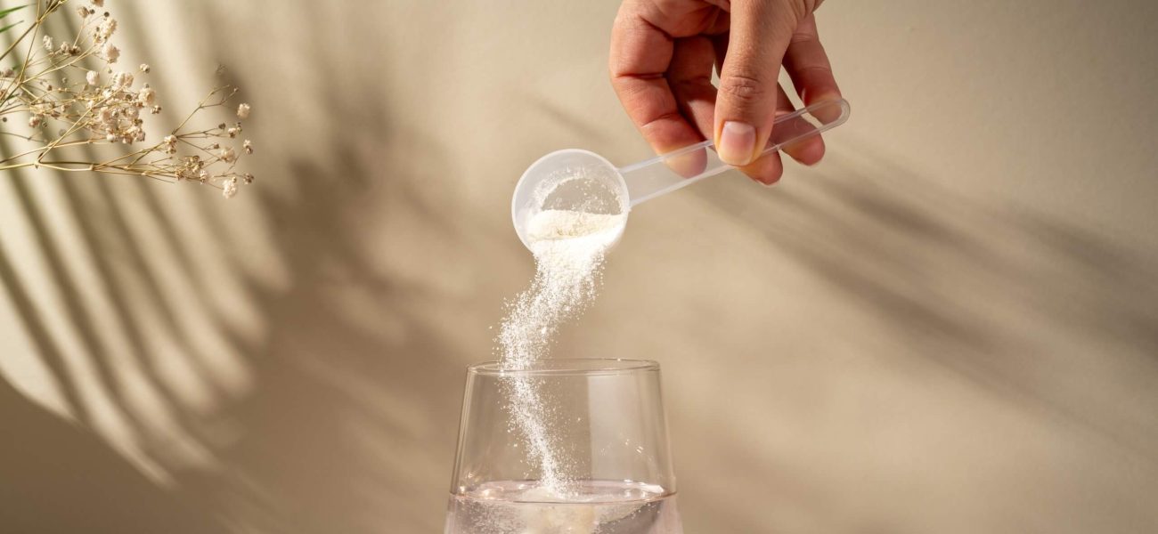 A spoon of collagen powder being added to a glass of water