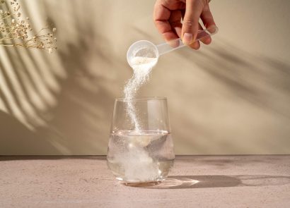 A spoon of collagen powder being added to a glass of water